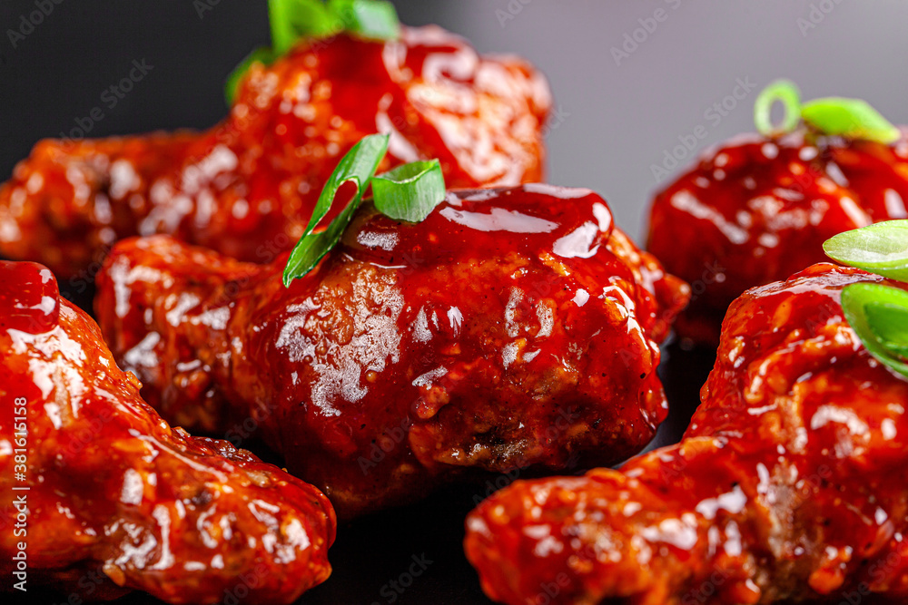 Obraz premium American cuisine. Chicken legs in sweet and sour sauce with green onions on a black background.