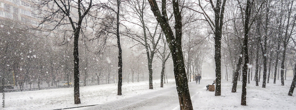 The first snow falls on a Park bench. Snow storm, snowstorm in the city. The first snow on a dark path and footprints on it. Heavy snowfall in the Park, large snowflakes fall on the sidewalk.