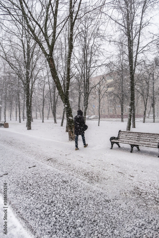 The first snow falls on a Park bench. Snow storm, snowstorm in the city. The first snow on a dark path and footprints on it. Heavy snowfall in the Park, large snowflakes fall on the sidewalk.