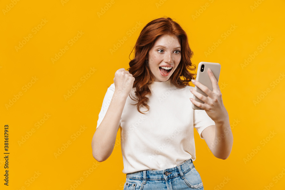 Image of ginger happy girl making winner gesture and using mobile phone Image of ginger happy girl making winner gesture and using mobile phone