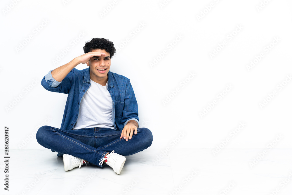 Venezuelan man sitting on the floor looking far away with hand to look something Venezuelan man sitting on the floor looking far away with hand to look something