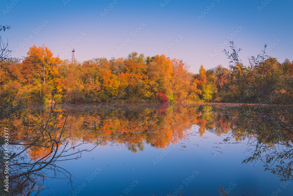 Obraz premium Colorful autumnal photo of a small lake, autumnal small lake with colorful trees in the background, reflections