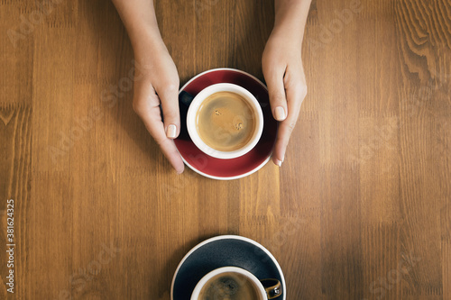 Female hands holding cup of coffee on wooden table as a background.