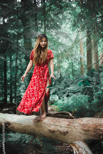 Beautiful Asian woman wearing red dress standing on a log in a forest