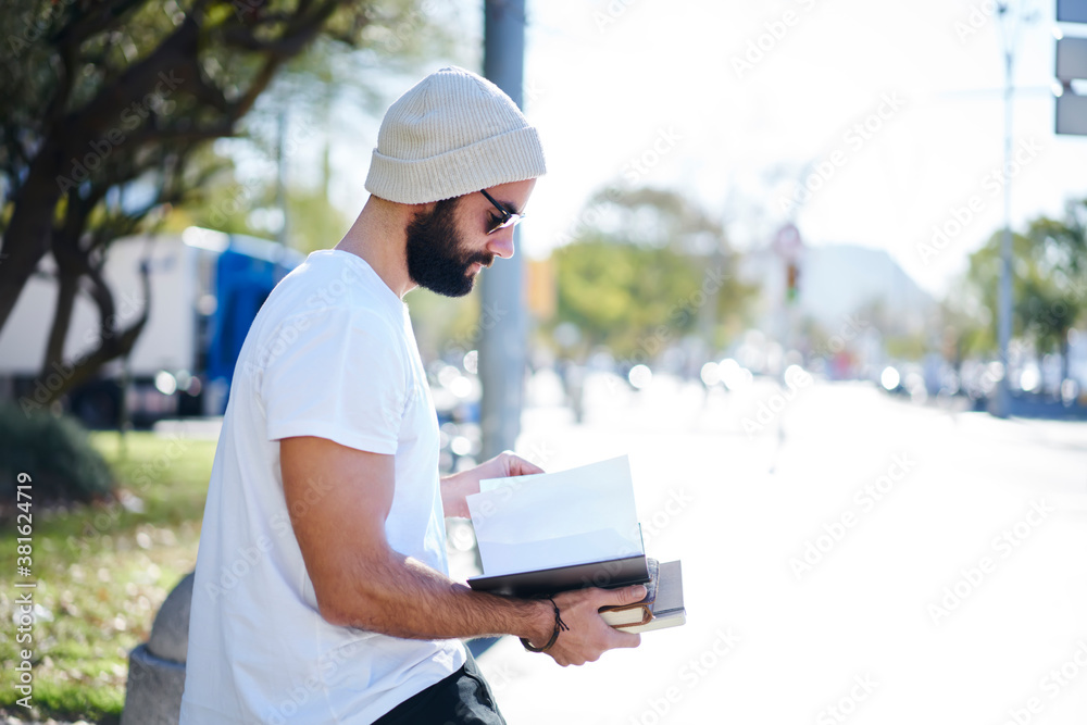 Serious young man with books standing on street Serious young man with books standing on street