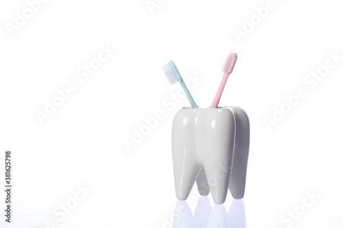 Two colorful toothbrushes in tooth-shaped holder. White decorative tooth, blue and pink toothbrushes. shiny toothbrush keeper isolated on white background copy space. Family without kids, childfree