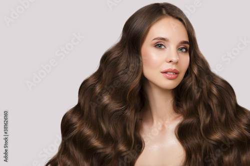Portrait of a beautiful brunette woman with wavy hair and makeup. On a gray background
