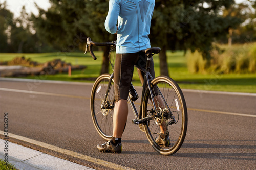 Rear view of athletic man in sportswear standing with bicycle on the road. Riding mountain road bike on a sunny summer day