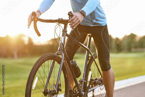 Cropped shot of professional road bicycle racer in sportswear cycling outdoors at sunset, man standing with bicycle on the road outdoors