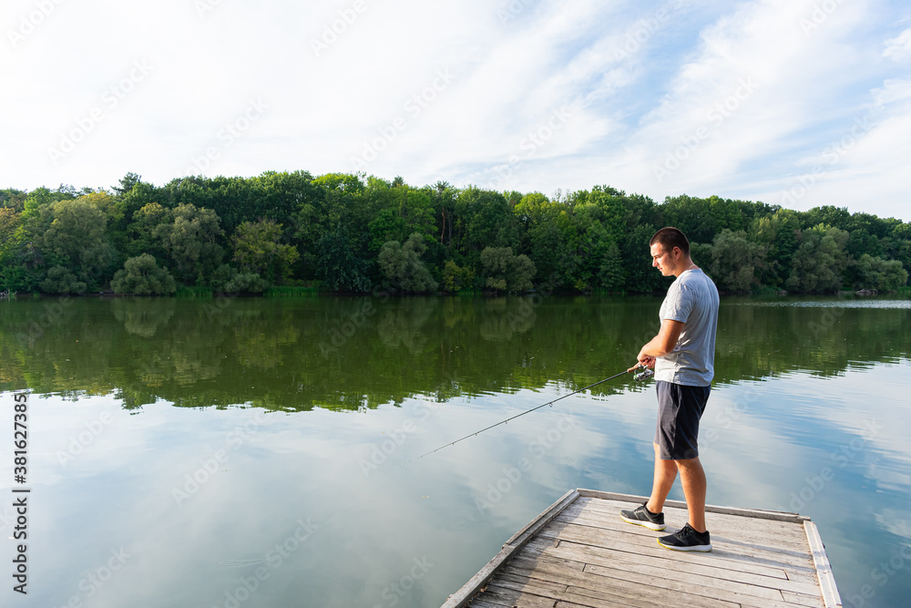 Fototapeta premium Man fishing on the pier. Fishing on the river on a sunny day. Autumn predator fishing