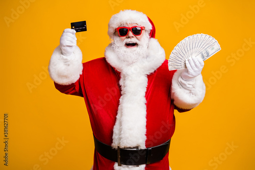 Portrait of his he nice attractive cheerful cheery glad fat overweight Santa holding in hand usd 100 salary deposit bank card isolated bright vivid shine vibrant yellow color background