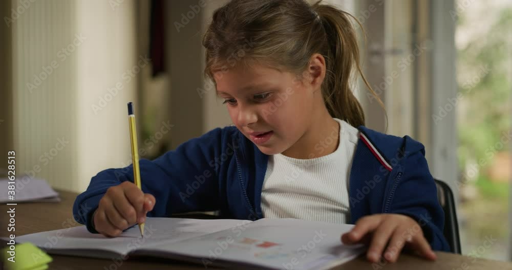 Authentic shot of little girl pupil is sitting at desk and writing in notebook while doing a homework to prepare for school day in her room at home. Concept: education,student, curiosity, family Authentic shot of little girl pupil is sitting at desk and writing in notebook while doing a homework to prepare for school day in her room at home. Concept: education,student, curiosity, family