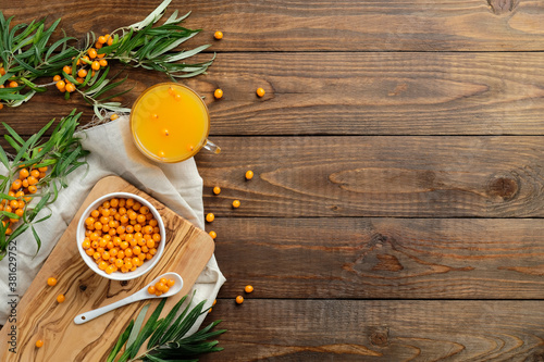Sea buckthorn berries, sea buckthorn juice and plant leaves on wooden desk. Flat lay composition, top view.