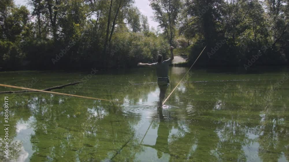 Caucasian man practicing slackline over the surface of the river in the forest. A man practices highlining over water in summer at dawn. Caucasian man practicing slackline over the surface of the river in the forest. A man practices highlining over water in summer at dawn.