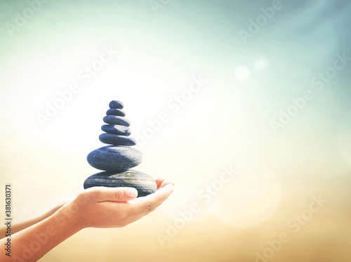 World philosophy day concept: Human hands holding balanced rocks over sunset beach background