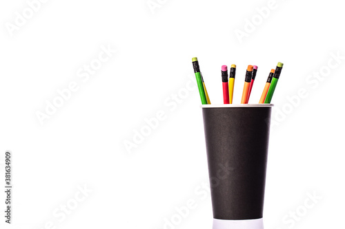 Bunch of multi colored wooden pencils with rubber eraser in black disposable biodegradable paper cup Copy space for advertisement isolated on white background. Recycling concept. Minimalism style.