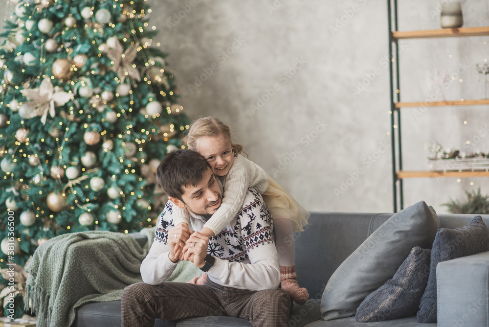 a dad anad a daughter sit on the sofa in christmas decorated living room