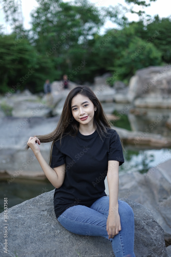 Stylish blonde girl wearing a black shirt with views of natural rocks, lake water and clear sky. female t-shirt models for mockups and templates. Stylish blonde girl wearing a black shirt with views of natural rocks, lake water and clear sky. female t-shirt models for mockups and templates.