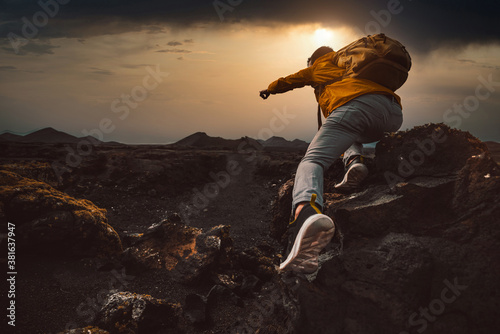 Successful hiker hiking a mountain pointing to the sunset. Wild man with backpack climbing a rock over the storm. Success, wanderlust and sport concept. photo
