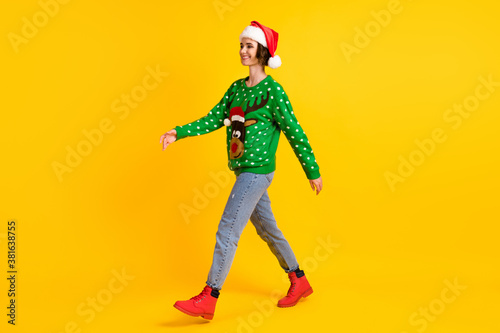 Full length profile side photo positive girl in santa claus headwear go walk copyspace x-mas christmas theme party wear deer decor sweater jeans boots isolated bright shine color background