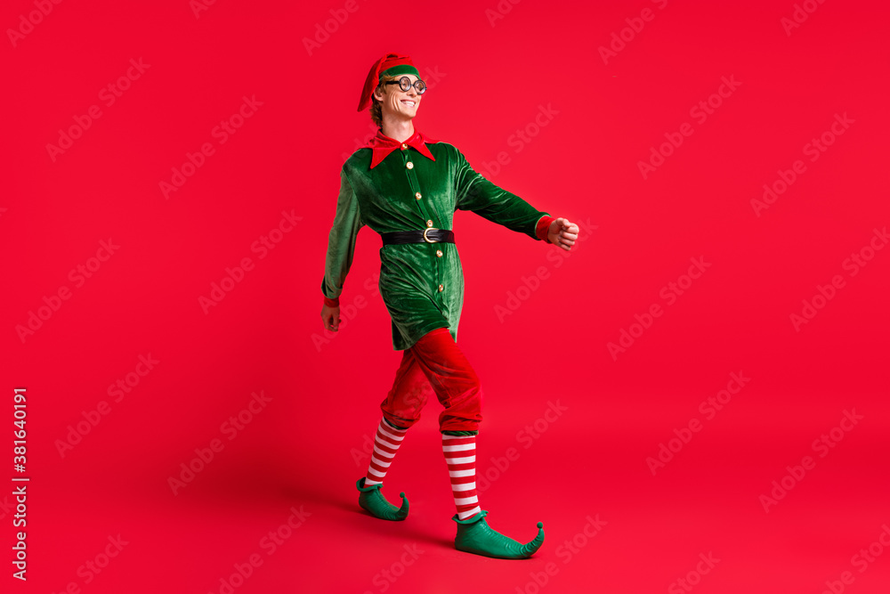 Full body photo of positive cheerful elf guy go copyspace isolated over red vibrant color background Full body photo of positive cheerful elf guy go copyspace isolated over red vibrant color background