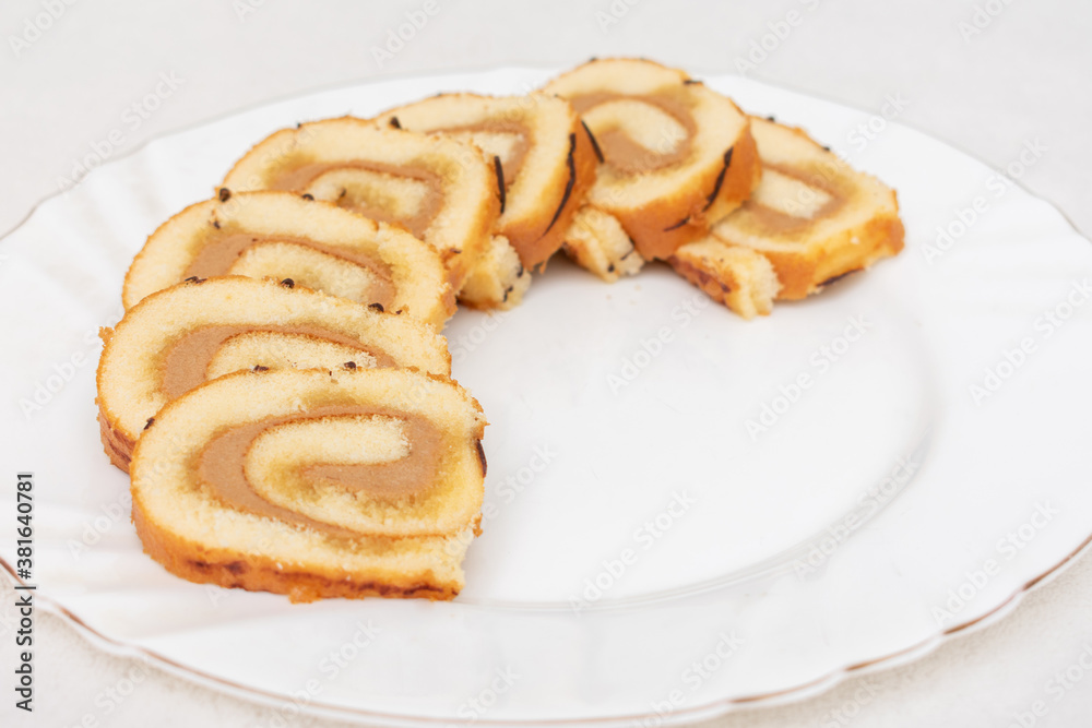 Delicious sponge roll cut into pieces on a white plate, top view, close-up Delicious sponge roll cut into pieces on a white plate, top view, close-up