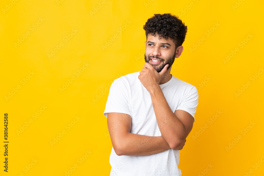 Young Moroccan man isolated on yellow background looking up while smiling Young Moroccan man isolated on yellow background looking up while smiling