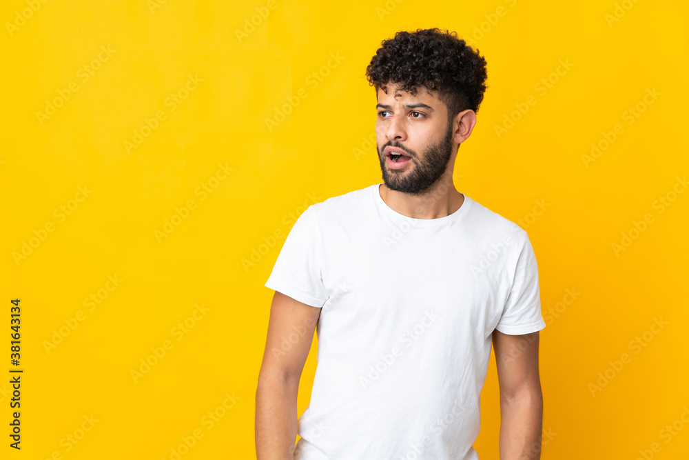Young Moroccan man isolated on yellow background doing surprise gesture while looking to the side Young Moroccan man isolated on yellow background doing surprise gesture while looking to the side