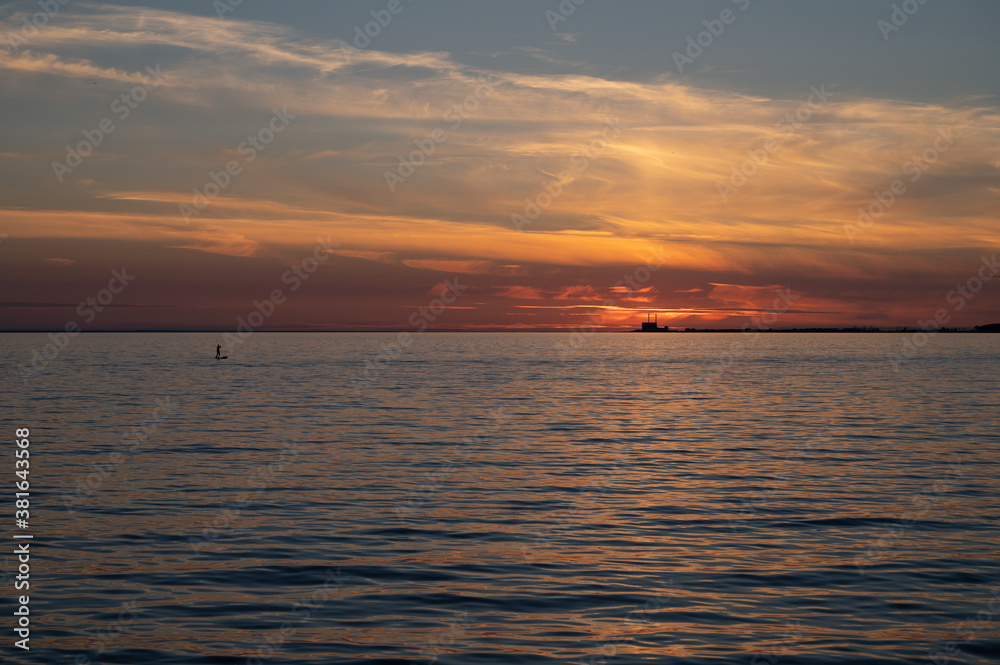 A man standing on a surf board on the calm bay water with the nuclear power plant Barsebäck visible on the horizon during summer in Sweden A man standing on a surf board on the calm bay water with the nuclear power plant Barsebäck visible on the horizon during summer in Sweden