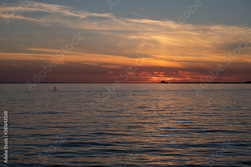 A man standing on a surf board on the calm bay water with the nuclear power plant Barsebäck visible on the horizon during summer in Sweden