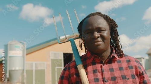 Happy african farmer holding fork over the soulder and nodding his head in front of the silo system . High quality 4k footage photo