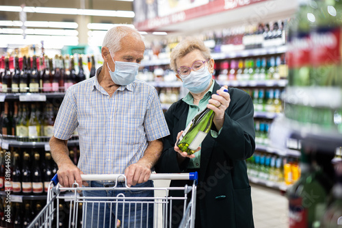 mature european spouses chooses bottle of wine in alcohol section of supermarket