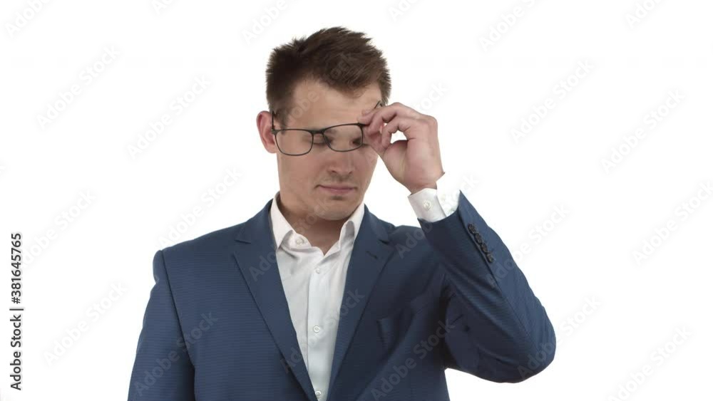 Handsome young businessman in blue suit, taking-off glasses and rubbing eyes, feeling tired from work, standing over white background