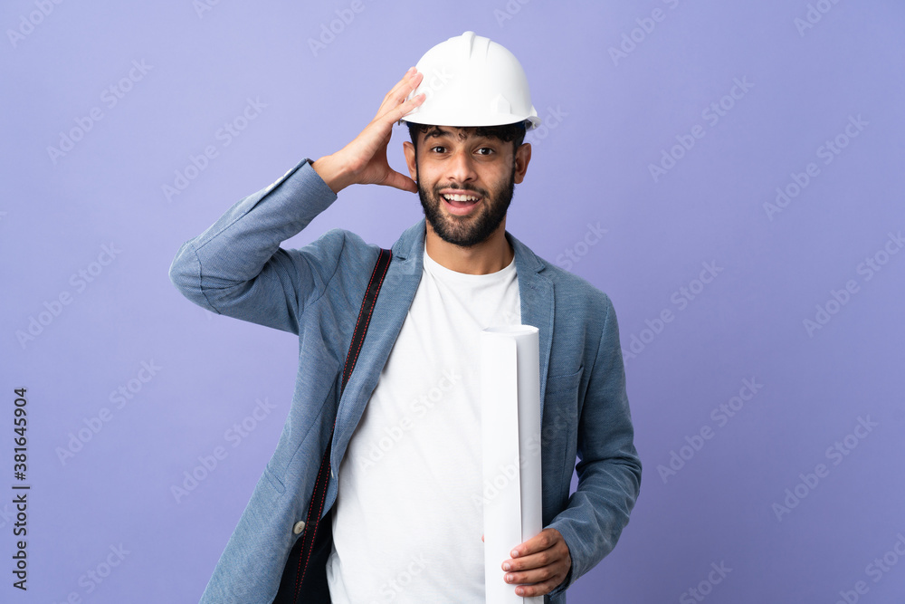 Young architect Moroccan man with helmet and holding blueprints over isolated background with surprise expression Young architect Moroccan man with helmet and holding blueprints over isolated background with surprise expression