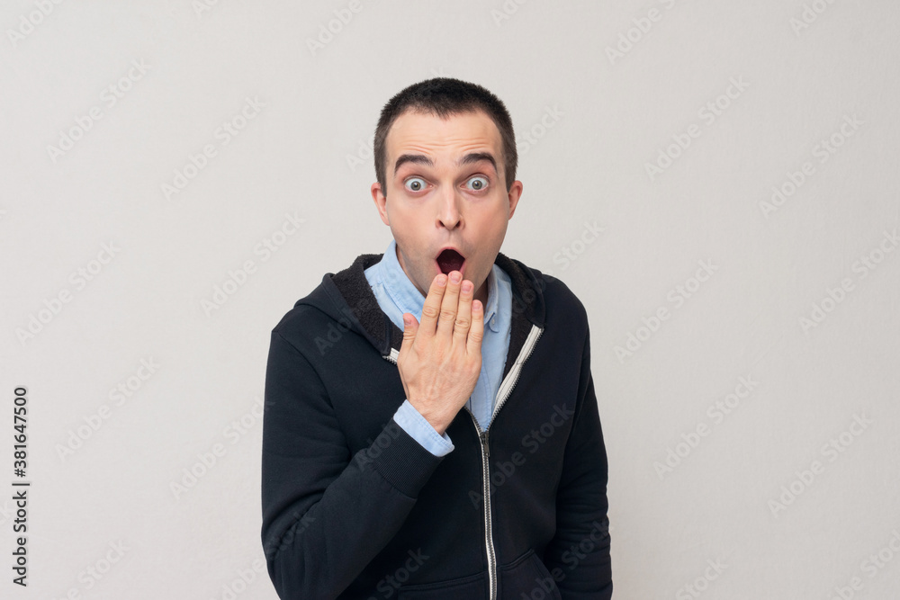 Shocked young man covering his mouth with hands, white background Shocked young man covering his mouth with hands, white background