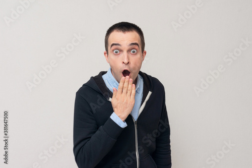 Shocked young man covering his mouth with hands, white background