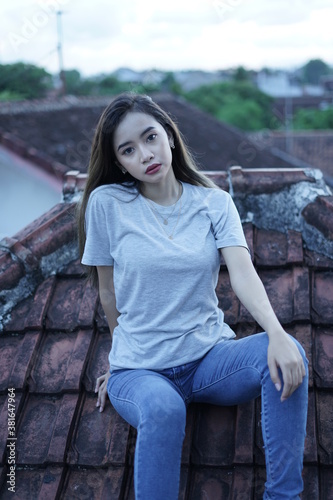 The blonde girl sits on the roof tile while stylishly wearing a gray shirt. female t-shirt models for mockups and templates.