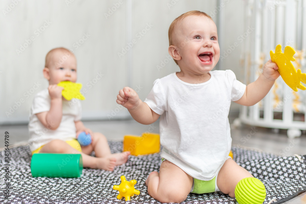 Cute baby laughs and plays with his friend in toys in the room while sitting on the floor Cute baby laughs and plays with his friend in toys in the room while sitting on the floor