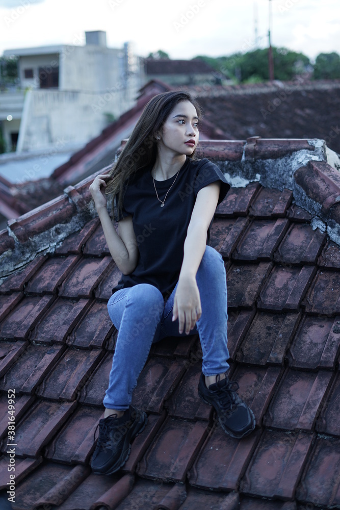 The blonde girl sits on the roof tile while stylish wearing a black t-shirt. female t-shirt models for mockups and templates.