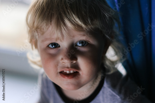 Soft focus portrait of a small curly haired blond boy looking at the camera.