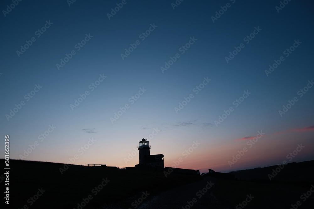 Silhouette of a lighthouse on a hill with light clouds and cool skies