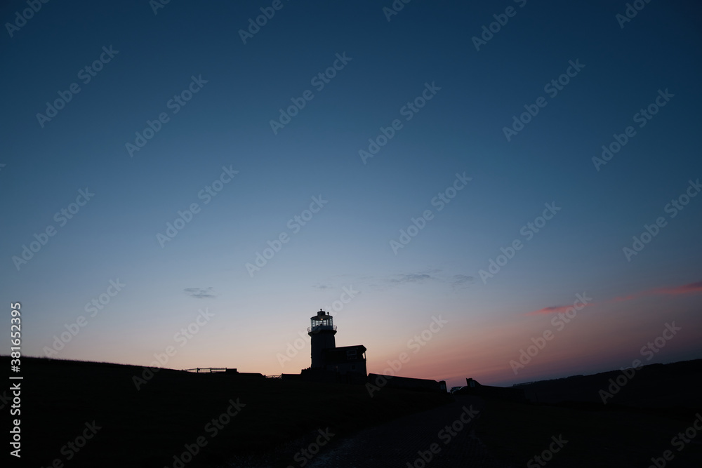 Silhouette of a lighthouse on a hill with light clouds and cool skies Silhouette of a lighthouse on a hill with light clouds and cool skies
