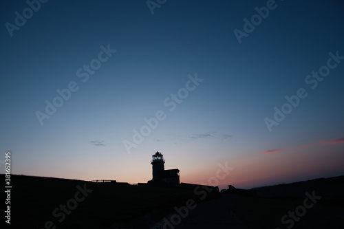 Silhouette of a lighthouse on a hill with light clouds and cool skies