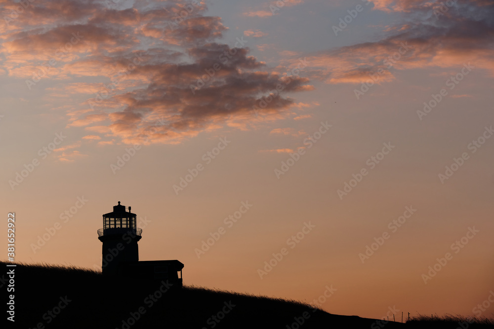 Silhouette of a lighthouse on a hill with light clouds and warm skies