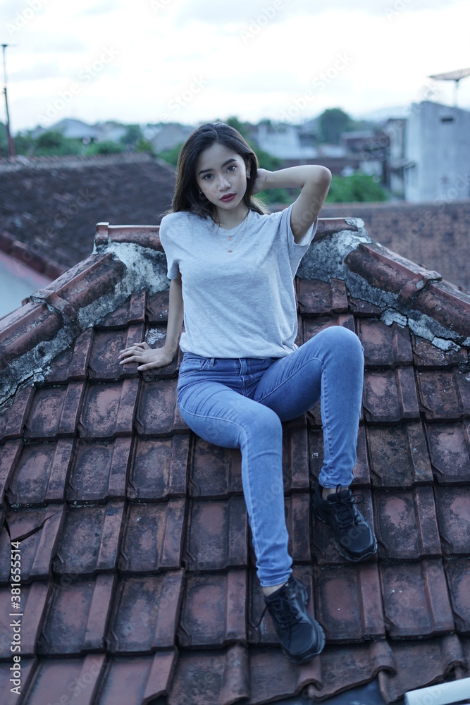 The blonde girl is sitting and stylish wearing a white T-shirt on the roof of the house with a view of the clear sky. female t-shirt models for mockups and templates.