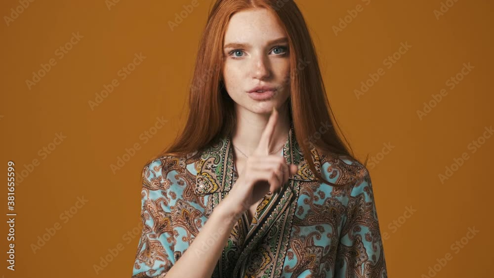 A serious young woman is doing silence gesture standing isolated over brown background A serious young woman is doing silence gesture standing isolated over brown background