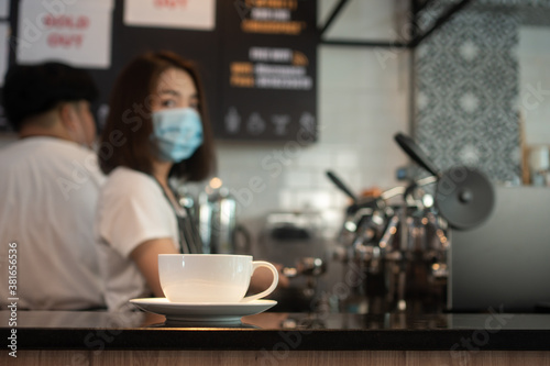 Selective focus of coffee cup and background of Asian barista woman wearing face masks To prevent contagious diseases And brewing coffee in the coffee shop. The concept of prevention from COVID 19