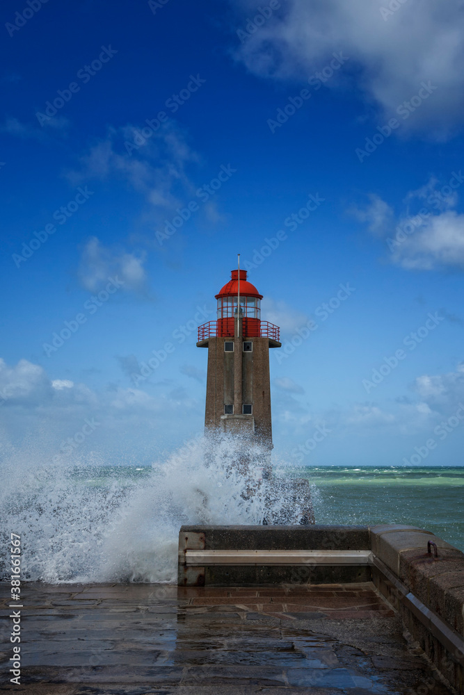 Waves crashing against the red beacon at the harbor entrance of Fécamp, France