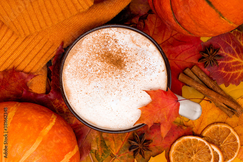 Colorful autumnal maple leaves with cup of spiced coffee, pumpkins and cozy sweater. Cappuccino with cinnamon and dried oranges top view. Autumn background.