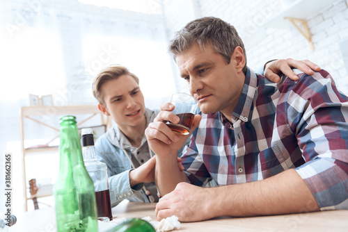 Father drinks alcoholic while son sits nearby.